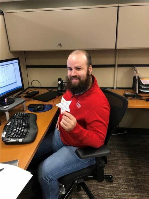 Smiling man with a beard holds a star-shaped award in an office setting, seated at a desk with a computer.