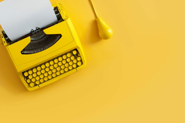 Bright yellow typewriter with a blank sheet of paper and a matching yellow power cord on a solid yellow background.