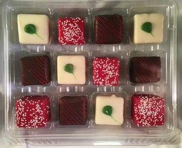 A tray of assorted chocolates featuring red, white, and dark varieties, some decorated with green accents and sprinkles.