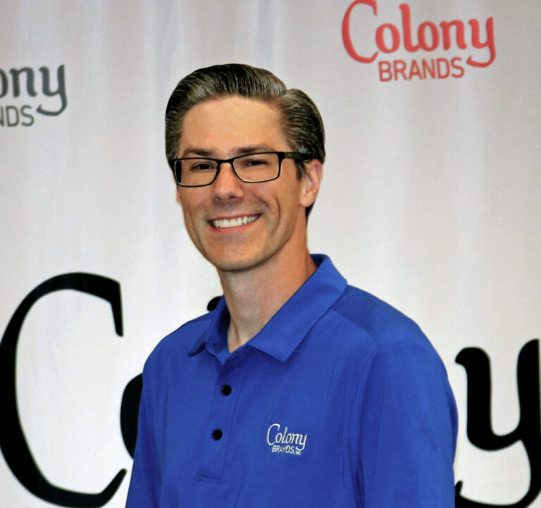 Smiling man in a blue polo shirt with "Colony Brands" logo, standing in front of a branded backdrop.