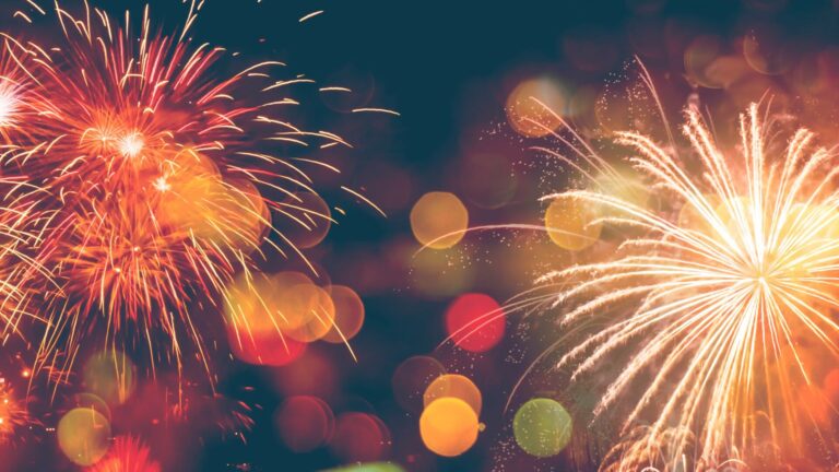 Colorful fireworks burst in the night sky, surrounded by vibrant bokeh lights in shades of red, orange, and yellow.